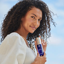 Woman holding a blue skincare bottle against a clear sky