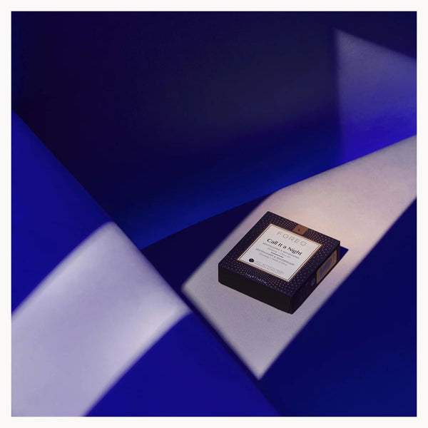 A small rectangular product box with a white label sits on a geometric blue and white surface. The box appears dark, likely black or very deep navy, with a textured pattern and a visible 'L'Or élixir' label.