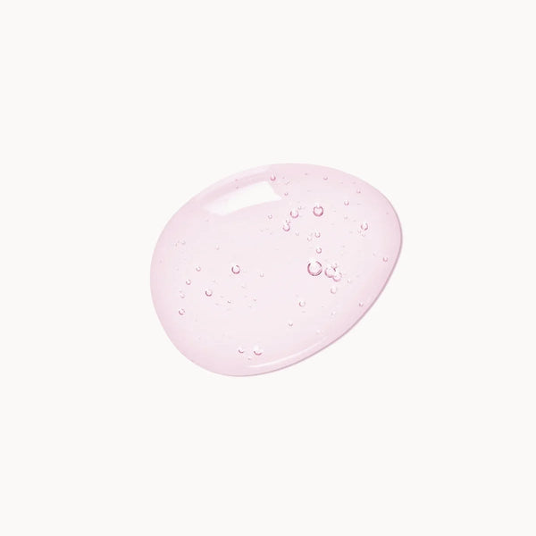 A glossy, translucent droplet of light pink cosmetic gel or serum with tiny air bubbles, centered on a solid off-white background.