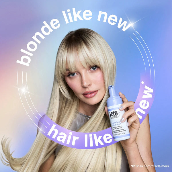 Woman with blonde hair holding a K18 hair product against a gradient blue background