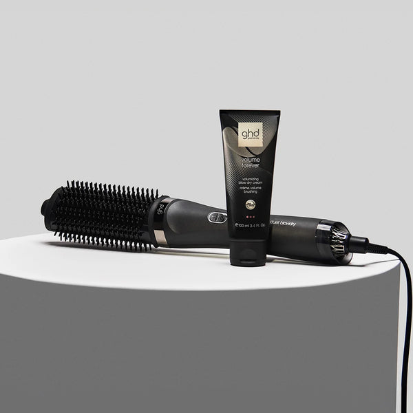 ghd styling tool and hair product on a white surface with a gray background