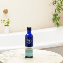 Neal's Yard Remedies Aromatic Foaming Bath bottle on a marble top next to a bath