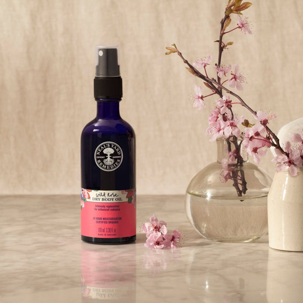 Neal's Yard Remedies Wild Rose Dry Oil next to a branch of small flowers