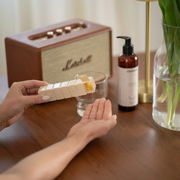 Person applying cream from a small container on a wooden table with a Marshall speaker and other items in the background.