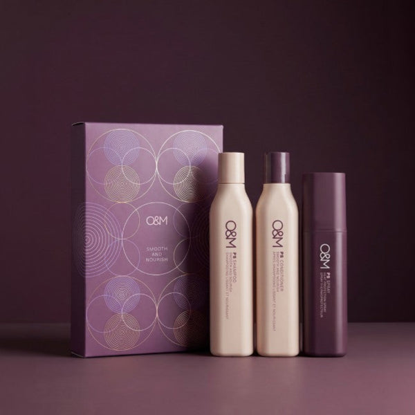 A Q&M hair care set featuring a purple gift box with gold concentric circle patterns, alongside three bottles and a jar in matching purple and cream tones, set against a dark purple background.