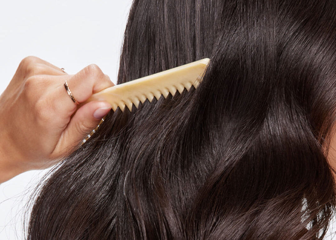 Person combing their wavy hair with a beige comb against a neutral background