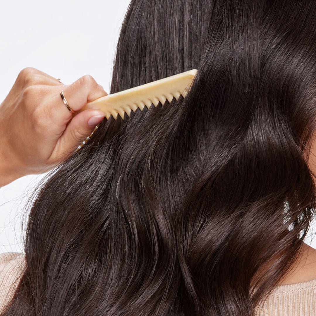 Person combing their wavy hair with a beige comb against a neutral background