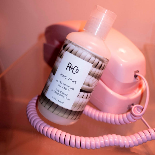 R+Co Ring Tone Ultra Defining Gel Crème placed in front of a phone