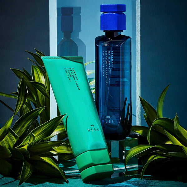 two bottles of R+Co Bleu Surreal Styling next to two plants