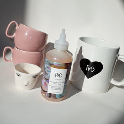 a bottle of R+Co Tea Cup Detox Rinse with 4 cups behind it