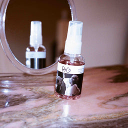 a bottle of R+Co Two Way Mirror Smoothing Oil on marble surface in front of a mirror