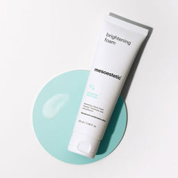 A tube of mesoestetic Brightening Foam on a green circle with a white background