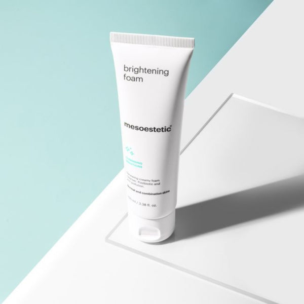 A tube of mesoestetic Brightening Foam on a glass slate and a green background
