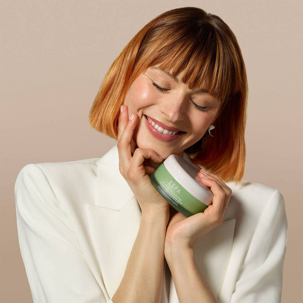 a women holding a tub to ESPA Tri-Active Regenerating Calming CICA Cleansing Balm to her face