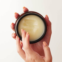 a hand scooping out the balm