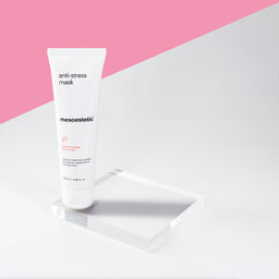 A tube of mesoestetic Anti-Stress Mask on a glass square on a pink background