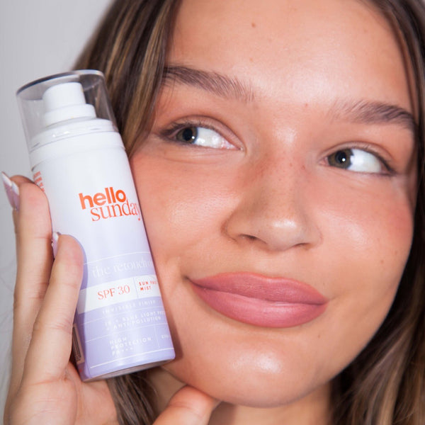 a closeup of a women holding a bottle of Hello Sunday The Retouch One - Face Mist SPF30 close to her face