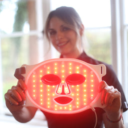a women holding a Deesse Pro Express LED Mask turned on showing its red lights