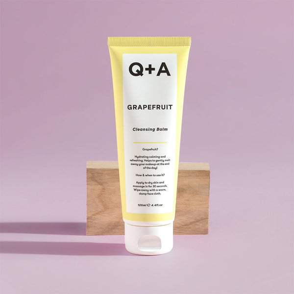 Q+A Grapefruit Cleansing Balm tube in front of a wooden block