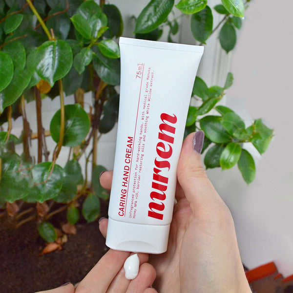 Nursem Caring Hand Cream Unfragranced applied to the fingertips of a hand in front of a plant