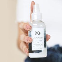 a bottle of R+Co Spiritualized Dry Shampoo Mist held to the camera