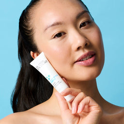 Model holding the firming serum bottle next to her cheek while looking into the camera