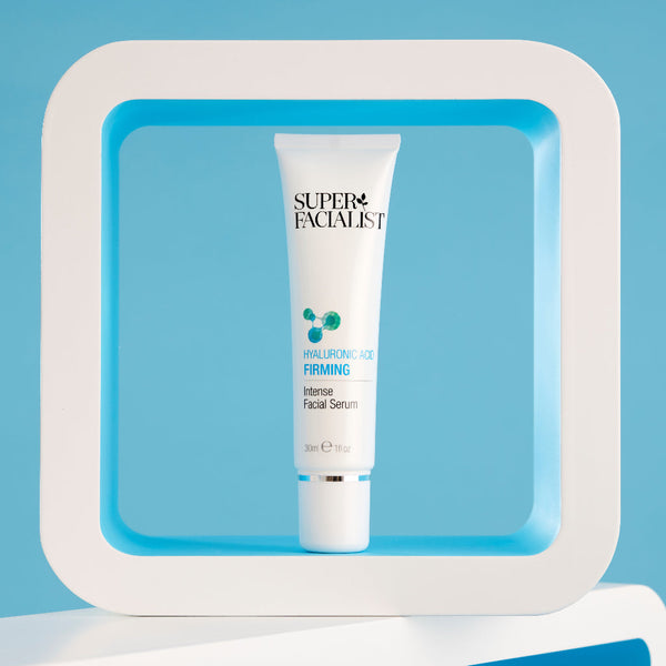 Firming facial serum tube inside a white square prop in front of a light blue background