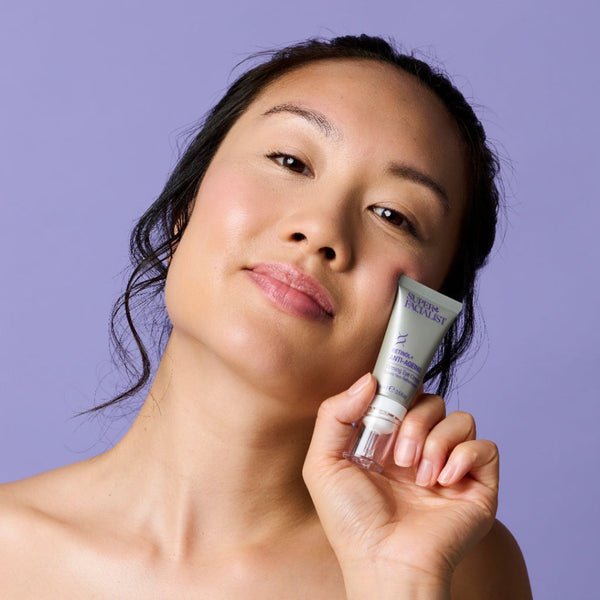 Model holding retinol eye cream next to her cheek while looking at the camera