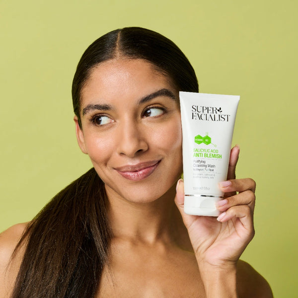 Model holding the salicylic acid cleansing wash tube next to her cheek while looking away