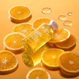 Vitamin C cleansing oil bottle on top of orange slices  and cleansing oil droplets