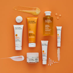 Super Facialit Vitamin C full range of skincare products on orange table with product textures around it