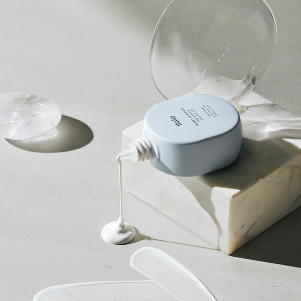 Huxley Sun Essence; Stay Sun Safe SPF50+on a marble cube, tipped over and spilling out